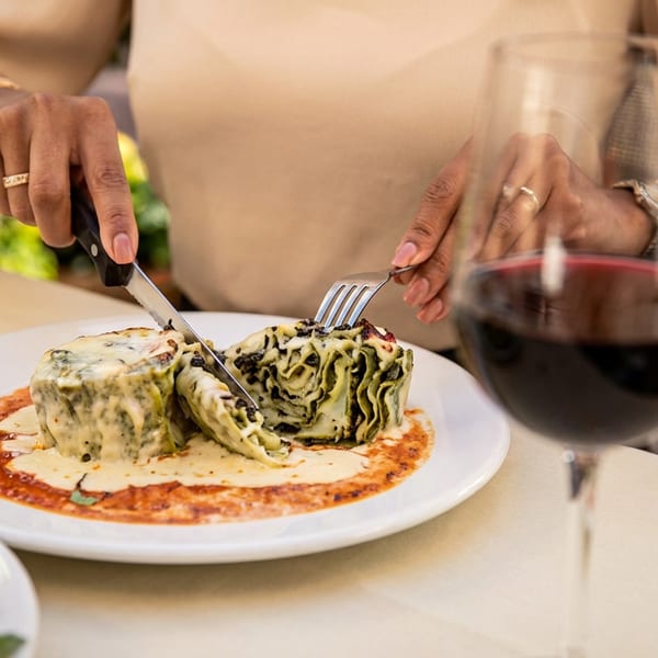 Diner cuts into layered spinach pasta topped with melted cheese, served in tomato cream sauce beside a glass of red wine.