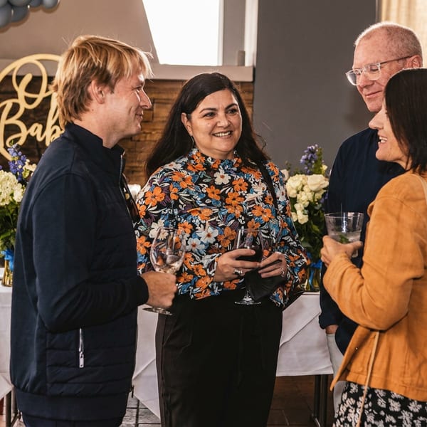 Guests socialize with drinks at a festive restaurant gathering decorated with balloon arches, flowers, and cocktail tables.